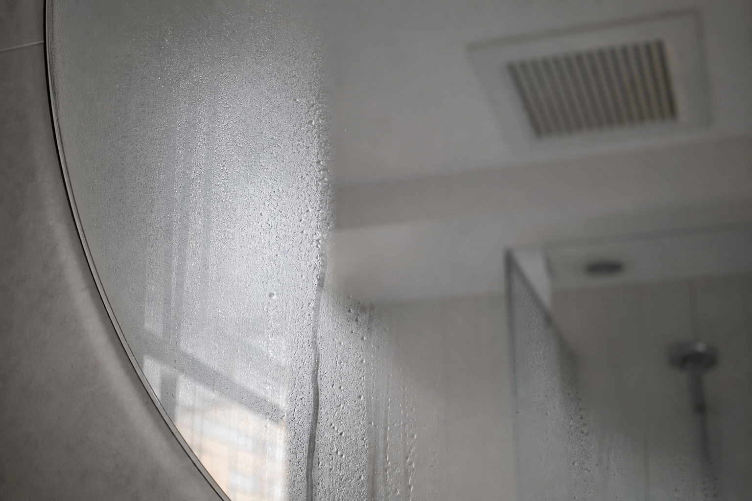 Miroir de salle de bain couvert de buée après une douche, grille de ventilation visible au plafond