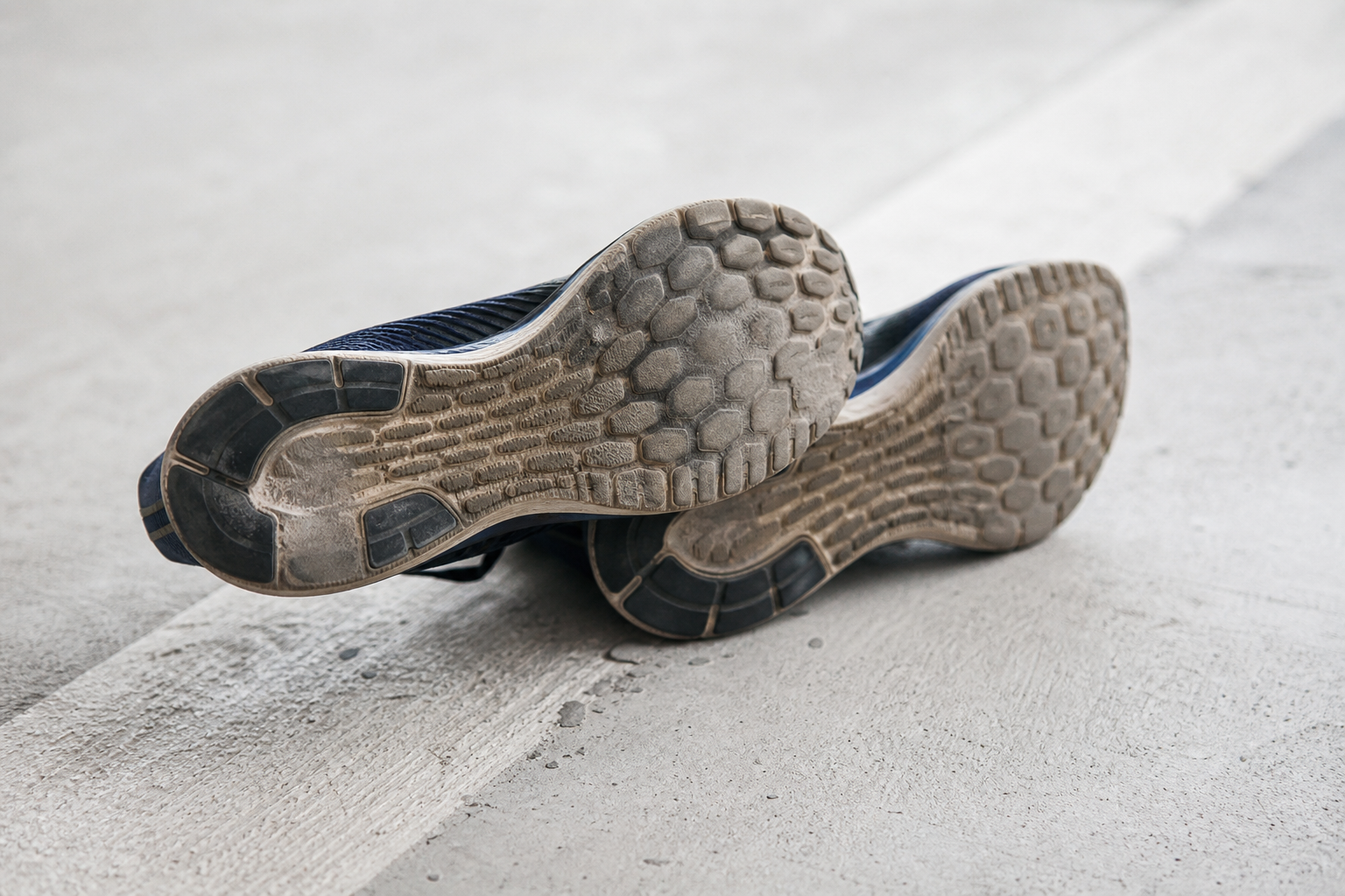Paire de chaussures de running posée au sol, semelle visible montrant une usure inégale