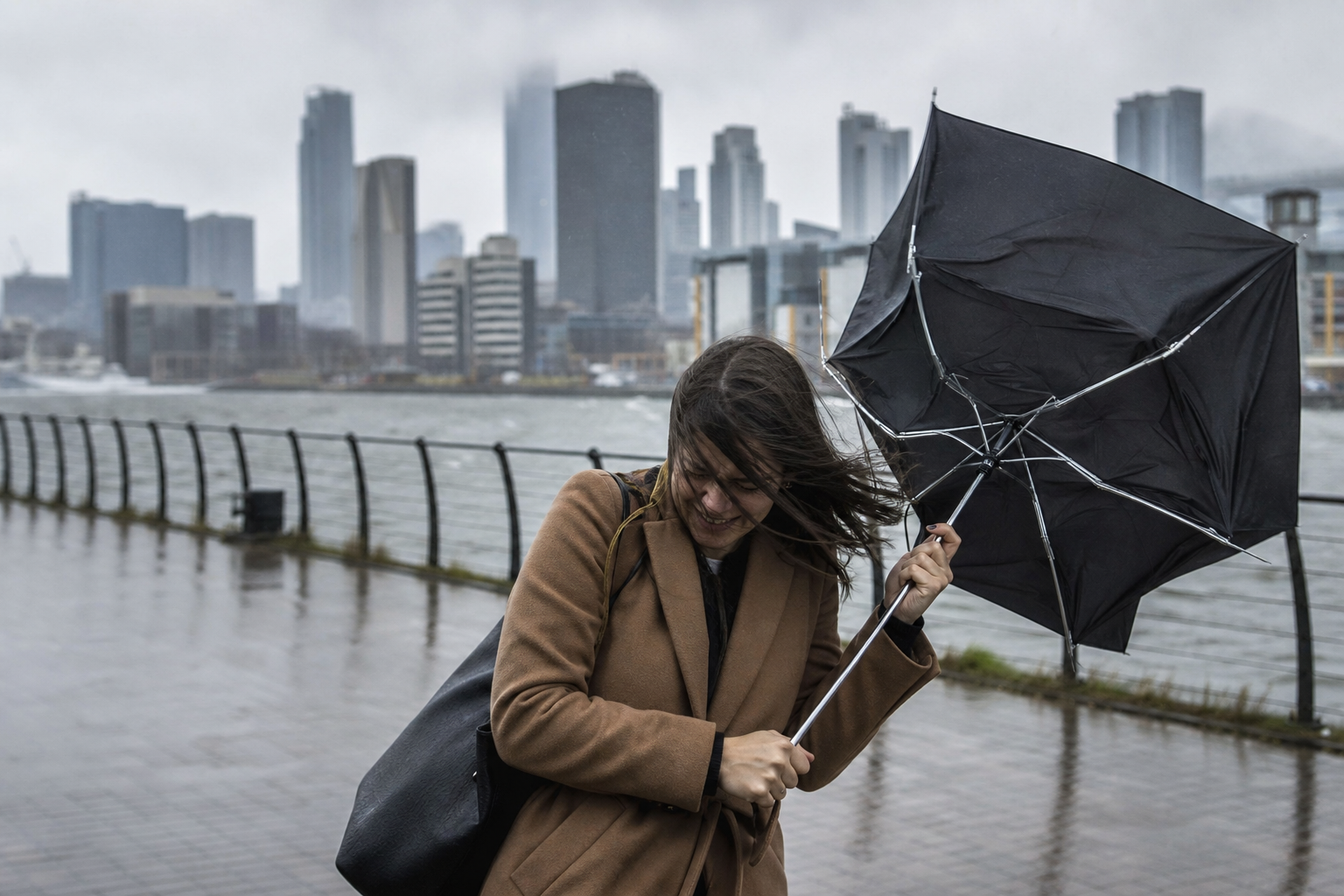 Personne dans la rue tenant un parapluie dont l’armature se retourne sous l’effet d’une rafale de vent